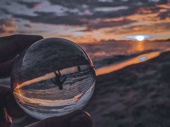 Cropped hand holding crystal ball at beach during sunset