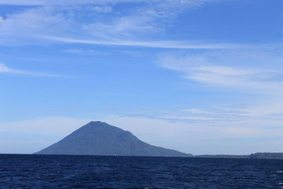 Scenic view of sea by mountain against sky