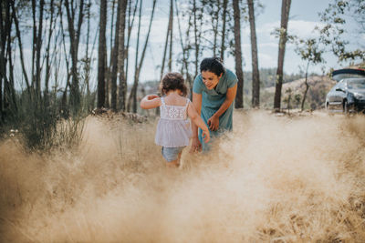 Mother and daughter on field against trees