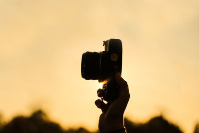 Cropped hand holding camera against orange sky