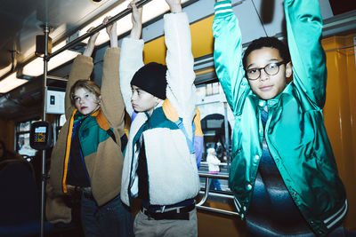 Male and female friends holding handle while traveling through tram during weekend