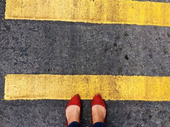 Low section of woman standing by yellow markings on road