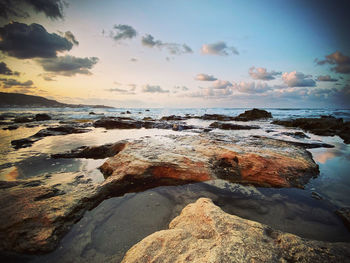 Rocks on shore against sky during sunset