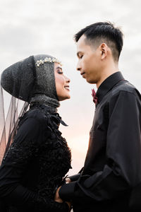 Side view of young couple standing against sky