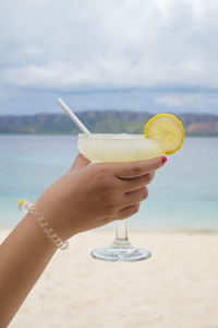 Midsection of man holding drink at beach