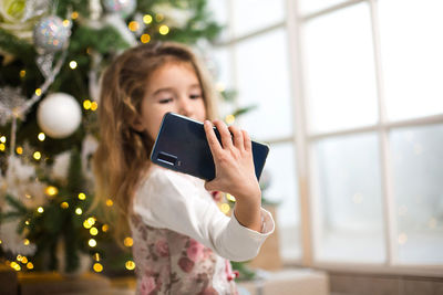 Girl holding mobile phone at christmas tree