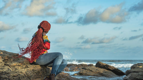 Rear view of woman sitting on rock at beach