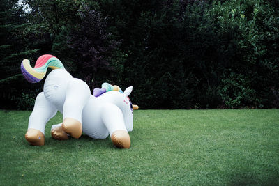 Rear view of inflatable unicorn laying on grass in front of trees