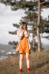 Midsection of woman holding camera while standing on field