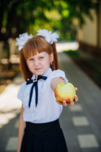 Back to school. a little schoolgirl stands in the school yard and holds an apple in her hands.