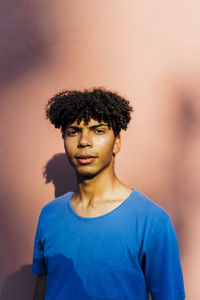 Young man with curly hair standing in front of coral wall