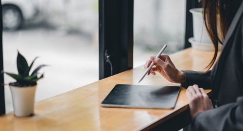 Midsection of woman using digital tablet at desk