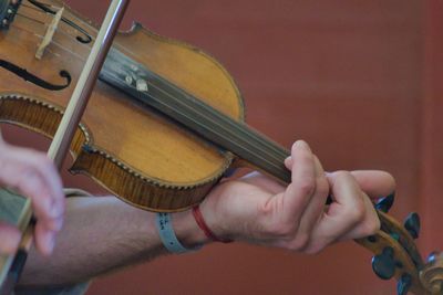 Cropped hand of man playing violin against wall