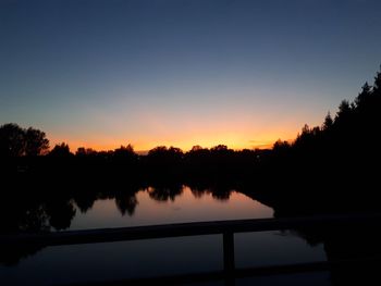 Silhouette trees by lake against sky during sunset