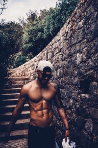 Shirtless young man walking by retaining wall