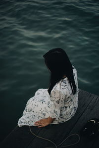 High angle view of woman sitting on jetty over sea