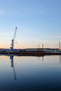 Construction site by sea against sky during sunset