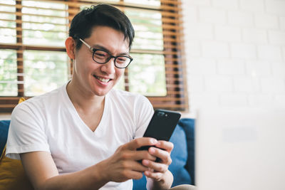 Smiling young man using phone while sitting on sofa at home