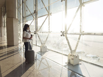 Young woman with suitcase talking on phone while waiting for flight