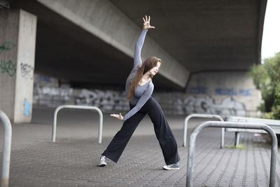 Young woman with arms raised dancing on footpath