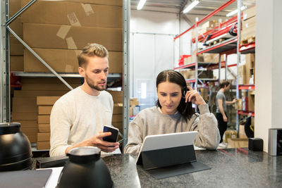 Colleagues discussing over digital tablet while standing in warehouse