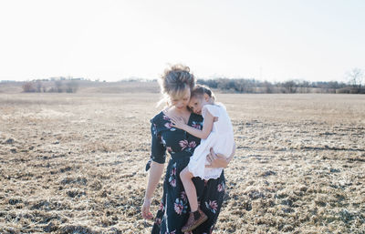 Mother holding her daughter walking through a filed at sunset