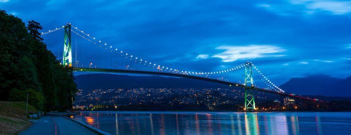 Illuminated suspension bridge over river against sky