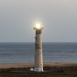 Lighthouse by sea against sky