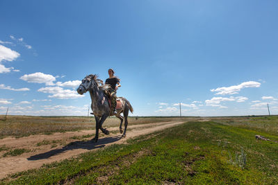 Woman riding horse on field against sky