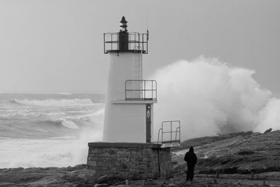 Person standing by lighthouse at beach against sky