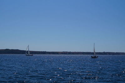 Sailboat sailing on sea against clear blue sky