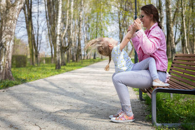 A mother cradles her daughter up and down while sitting on a bench in a city park.