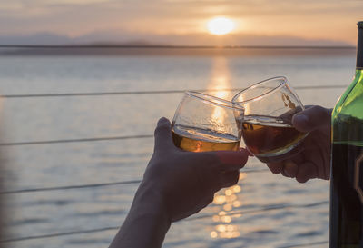 Cropped hands of friends toasting glasses during sunset against beach