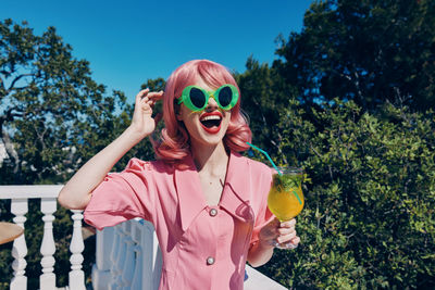 Portrait of young woman wearing sunglasses while standing against blue sky