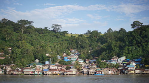 Scenic view of river amidst trees and buildings against sky