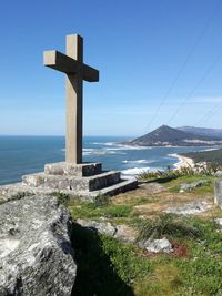 Cross on sea shore against sky