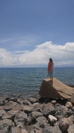 Rear view of man standing at beach against sky