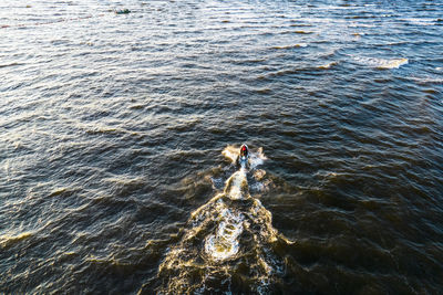 Aerial view of man rides on fast water scooter jumping on waves and making golden splashes on sunset 