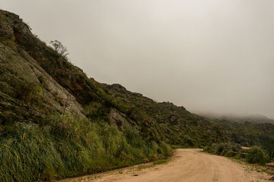 Dirt road by mountain against clear sky