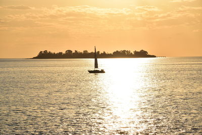 Sailboat sailing in sea against orange sky