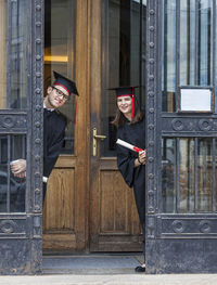 Portrait of friends in graduation gown standing at entrance of university