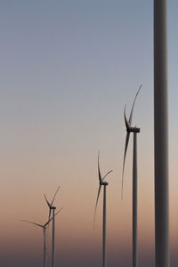 Low angle view of wind turbines against sky during sunset