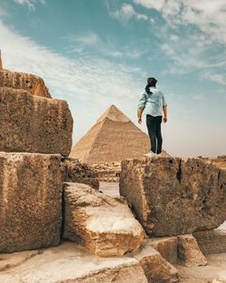 Rear view of man standing on rock against sky