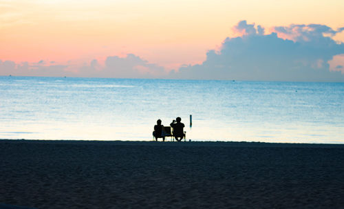 Silhouette people on beach against sky during sunset