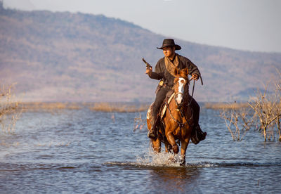 Man holding gun while riding horse in lake