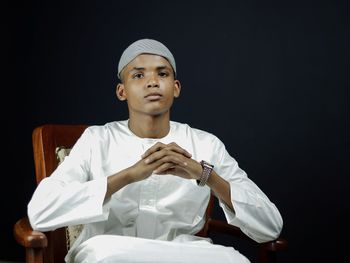 Low angle view of young man sitting against black background