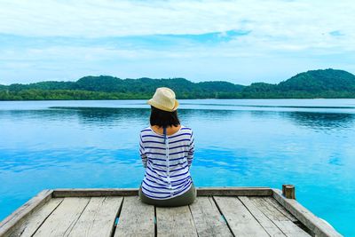 Rear view of woman sitting by lake against sky