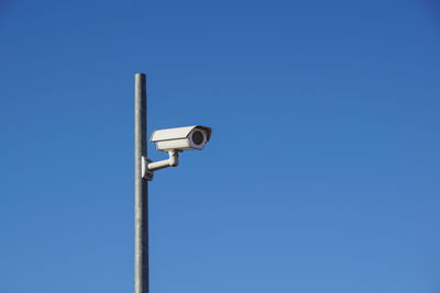 Low angle view of security camera on pole against clear blue sky