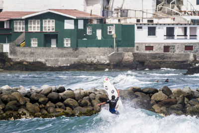 Rear view of man surfboarding on groyne in sea