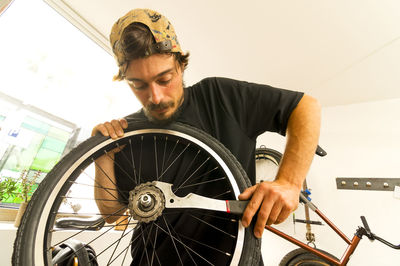 Low angle view of young man repairing bicycle wheel in workshop